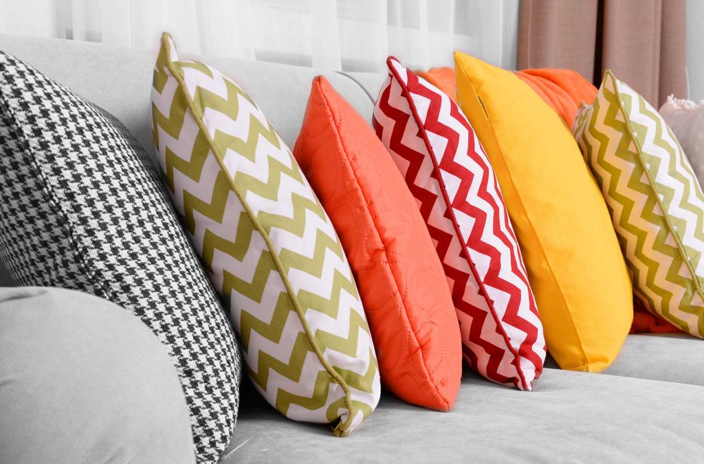 An image of workroom pillows in various colors placed on a couch